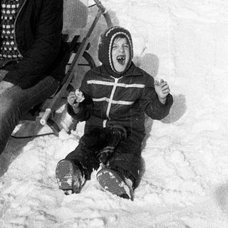 Two people sledding down snow-covered hill.
