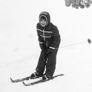 Child skiing on snow near building.