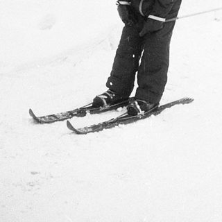 Child skiing on snow near building.