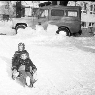 Children sledding down snow-covered hill.