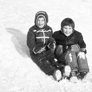 Two children sledding down snow-covered slope.