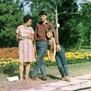 Family posing outdoors in colorful park flowers.