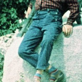 Person sitting on rocks in wooded outdoor area.