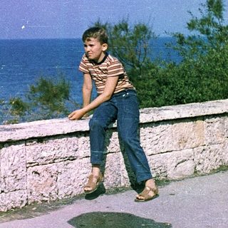 Boy leaning on stone wall near ocean.
