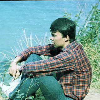 Young man sitting by water, deep in thought.