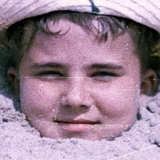 Child peeking out from sand with straw hat.
