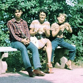 Three people sitting on bench outdoors, smiling.