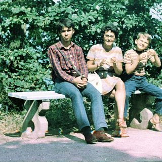 Three people sitting on bench outdoors, smiling.