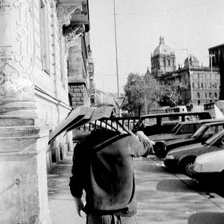 Man walking with umbrella and backpack near historic building.
