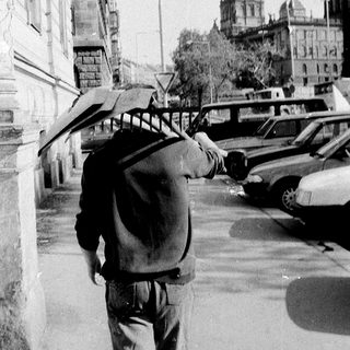 Man walking with umbrella and backpack near historic building.