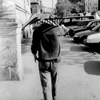 Man walking with umbrella and backpack near historic building.