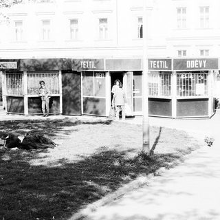 Vacant textile shops with boarded windows, two people standing outside.