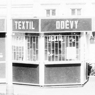 Vacant textile shops with boarded windows, two people standing outside.