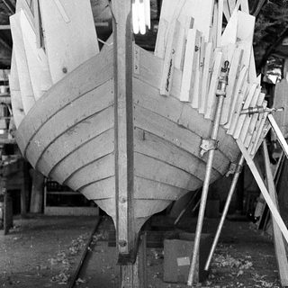 Half-built wooden boat hull in construction dock.