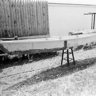 Old wooden boat on grass near shed.