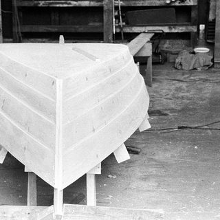 Unfinished wooden boat hull in workshop.