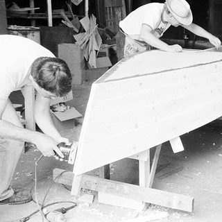 Three men building wooden boat hull together.