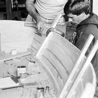Two people assembling wooden furniture using hand tools.