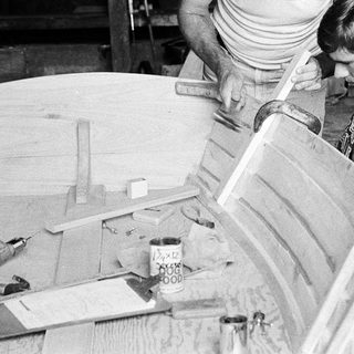 Two people assembling wooden furniture using hand tools.