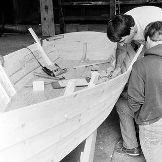 Two men building wooden boat hull.