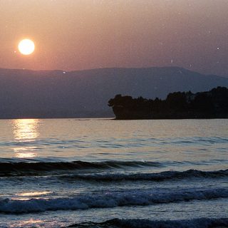 Sunset over calm ocean with distant land.