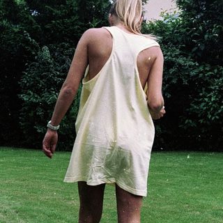 Woman in sleeveless dress walking barefoot on grass.
