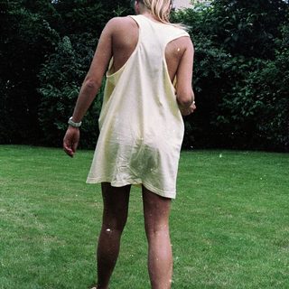 Woman in sleeveless dress walking barefoot on grass.