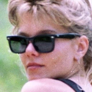 Woman wearing sunglasses and black top in grassy field.