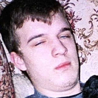 Teen holding game controller, lounging drowsily in armchair.