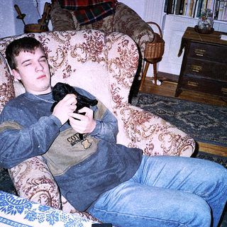 Teen holding game controller, lounging drowsily in armchair.
