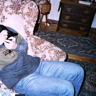 Teen holding game controller, lounging drowsily in armchair.