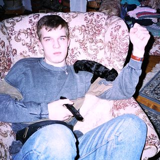 Young man playing video game with dog on lap.