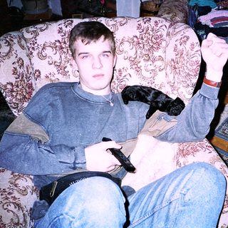 Young man playing video game with dog on lap.