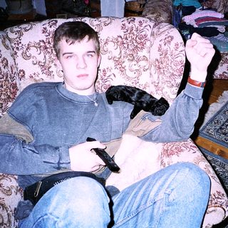 Young man playing video game with dog on lap.