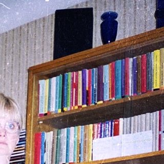 Person standing indoors holding a knife near kitchen shelves.