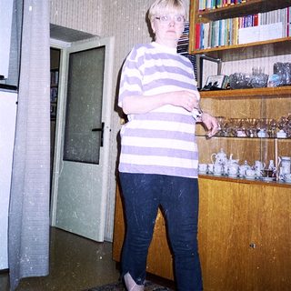 Person standing indoors holding a knife near kitchen shelves.
