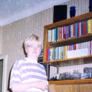 Person standing indoors holding a knife near kitchen shelves.