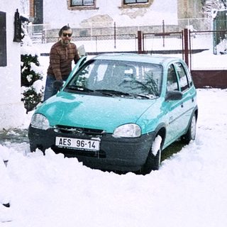 Snowy residential street with parked car and person near house.