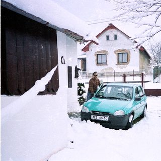 Snowy residential street with parked car and person near house.