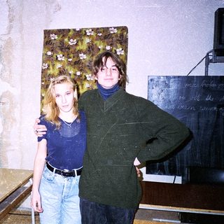 Two people posing indoors in casual 1990s attire.