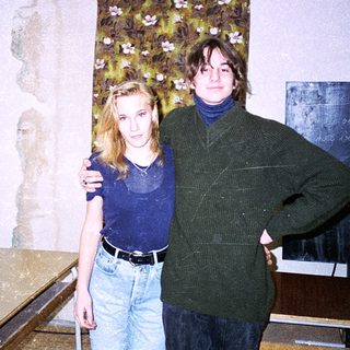 Two people posing indoors in casual 1990s attire.
