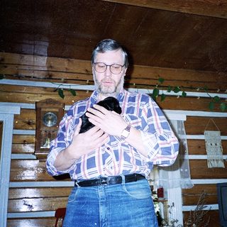 Man holding black cat indoors near wooden wall.