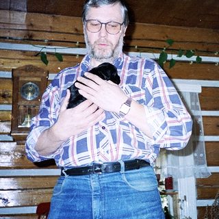 Man holding black cat indoors near wooden wall.