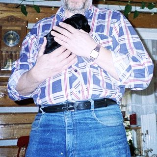 Man holding black cat indoors near wooden wall.