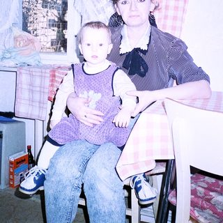 A woman holding a baby indoors near a poster of the Eiffel Tower.