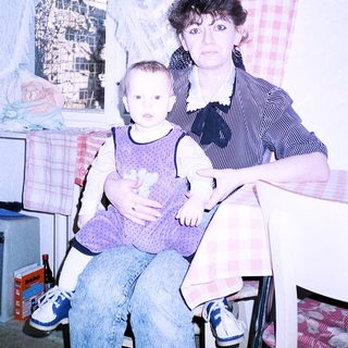 A woman holding a baby indoors near a poster of the Eiffel Tower.