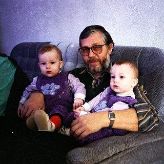 Man holding two young children on a couch.