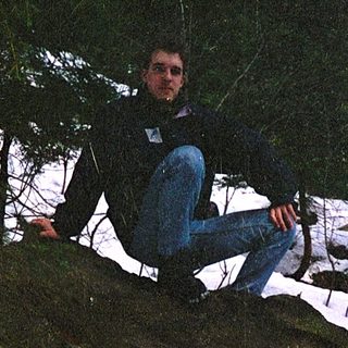 Person sitting on moss-covered rock in snowy forest.