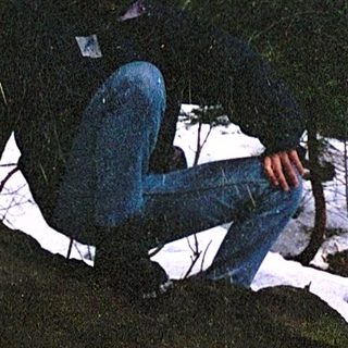 Person sitting on moss-covered rock in snowy forest.