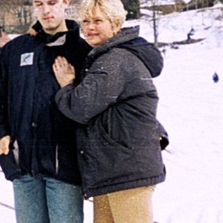 Two people embrace on snowy slope near village.